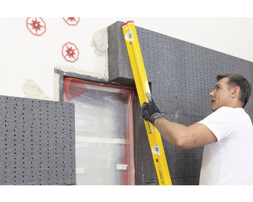 Mann verwendet eine Wasserwaage, um eine Dämmplatte aus Polystyrol an einer Hauswand anzubringen.