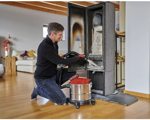 Ein Mann reinigt einen Kaminofen mit einem Aschesauger in einem Wohnzimmer.