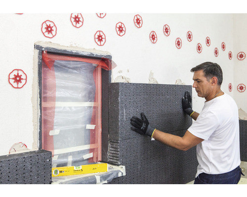 Mann befestigt Wärmedämmplatten an der Wand neben einem Fenster. Auf der Wand sind Dämmstoffdübel angebracht.