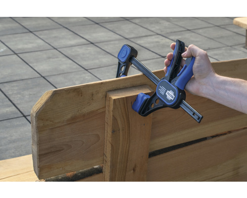 Hand hält eine Einhandzwinge an Holz