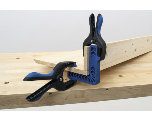 Zwei Holzstücke werden mit einer Winkelklemme und Federzwingen auf einer Werkbank fixiert.