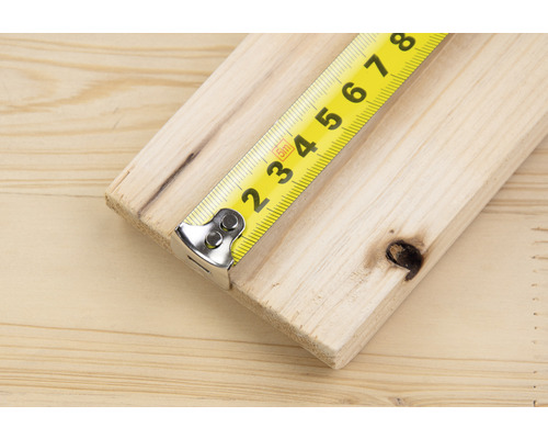 Gelbes Rollbandmaß misst ein Holzbrett.