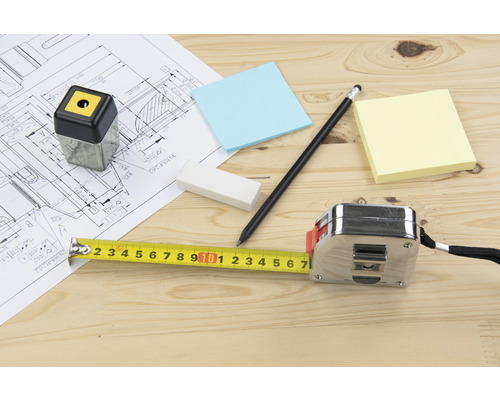 Bauplan mit Zollstock, Bleistift, Radiergummi, Notizzetteln und Spitzer auf einem Holztisch