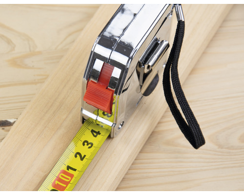 Ein Rollbandmaß liegt auf einem Holzbrett.