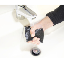 Eine Hand hält einen Schleifschwamm unter einen Wasserhahn in einem Waschbecken.
