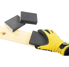 Eine Hand mit einem gelben Handschuh schleift ein Holzbrett mit einem Schleifblock, weitere Schleifblöcke liegen bereit.