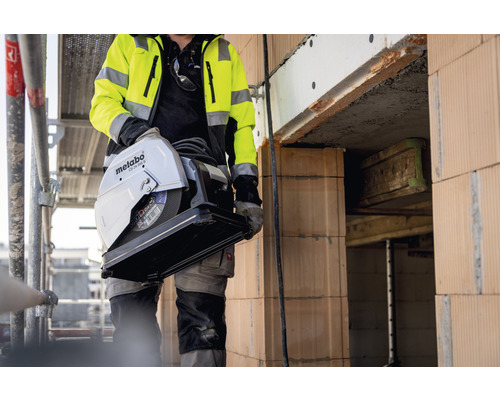 Ein Bauarbeiter trägt eine Metabo CS 23-355 S Metalltrennsäge auf einer Baustelle.