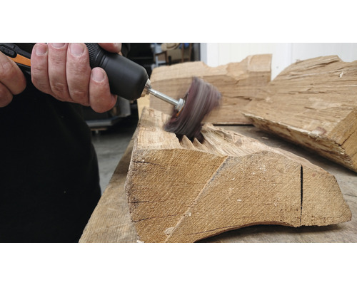 Eine Person benutzt eine rotierende Bürste, um ein Stück Holz zu bearbeiten.