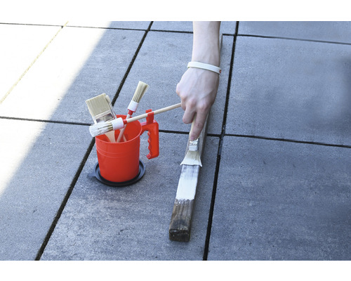 Farbeimer mit verschiedenen Pinseln und Anstrich eines Holzstücks