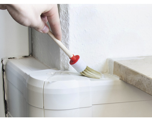 Eine Person streicht mit einem runden Pinsel eine Ecke.