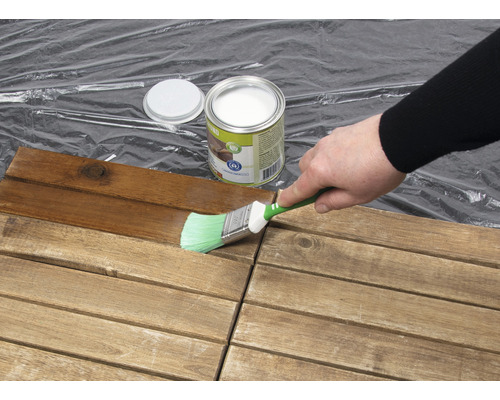 Eine Person streicht Holzfliesen mit einem Pinsel und Holzschutzlasur.