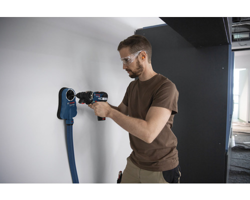 Ein Mann bohrt mit einem Akkuschrauber ein Loch in eine Wand, wobei ein Staubabsaugungsgerät von Bosch verwendet wird