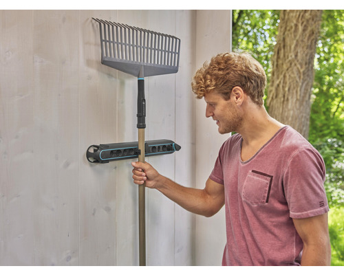 Eine Rechen hängt an einer Gerätehalterung an der Wand.