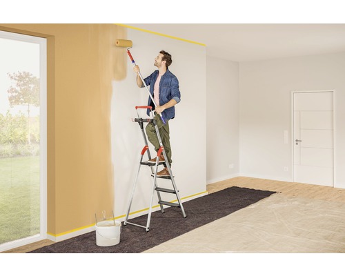 Mann streicht Zimmerwand mit Farbroller von einer Leiter aus