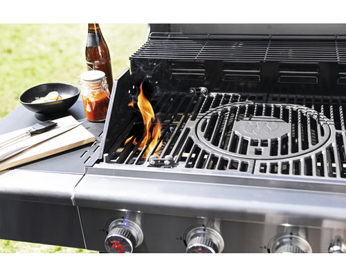 Grill mit Flammen, Soße, Bier und Grillzubehör auf einem Tisch