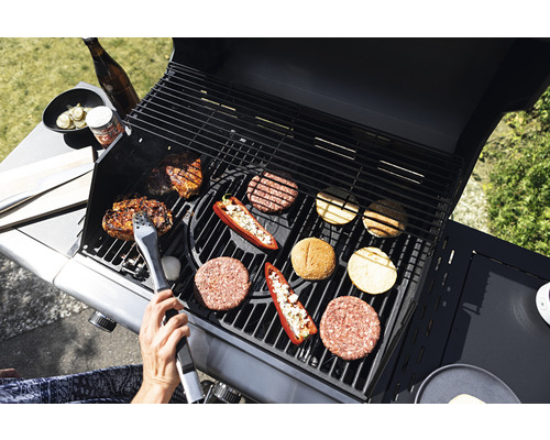 Grillszene mit Fleisch, Burger-Patties und Gemüse auf einem Grill mit Grillzange.