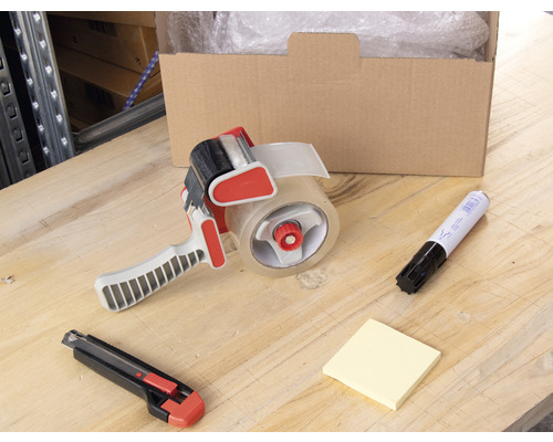 Szene mit einer geöffneten Kiste, Luftpolsterfolie, einem Klebebandabroller, einem Cutter, einem Markierstift und Notizzetteln auf einem Tisch.