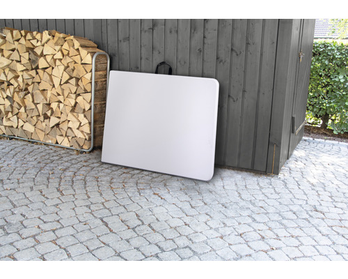 Weißer Klapptisch im Freien, neben Holzstapel und Holzhütte