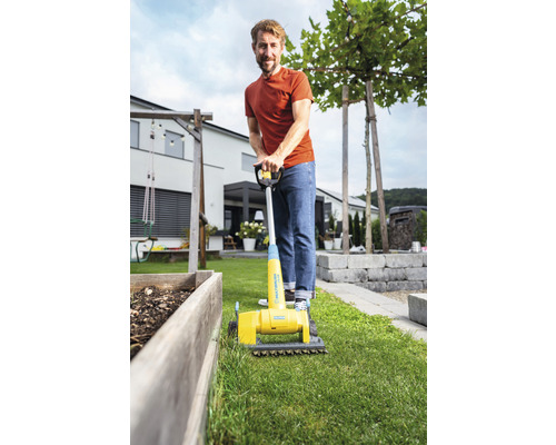 Mann benutzt einen gelben Vertikutierer im Garten.