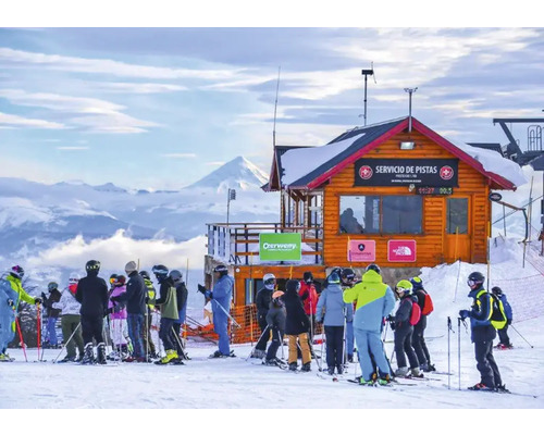 Skifahrer stehen vor einer Holzhütte mit der Aufschrift Service de Pistas auf einer schneebedeckten Berglandschaft