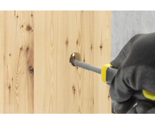 Eine Person vergrößert mit einer Holzraspel ein Loch in einem Holzbrett.