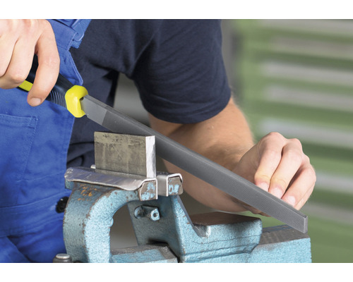 Person feilt Metallstück im Schraubstock mit einer Metallfeile