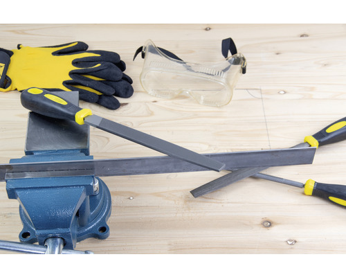 Werkstattszene mit Schraubstock, Feilen, Schutzbrille und Arbeitshandschuhen auf einer Holzoberfläche