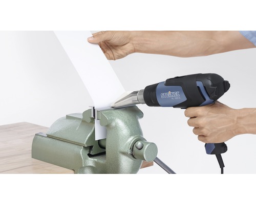 Eine Person erhitzt ein Werkstück mit einem Heissluftfön, das in einem Schraubstock eingespannt ist.