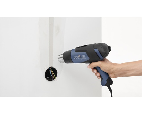 Eine Person verwendet eine Heißluftpistole von Steinel, Modell HL 1620 S, an einer Wand mit einer Stromdose