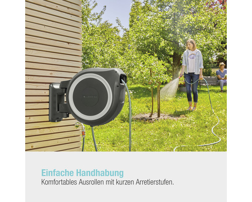 Gardena Schlauchbox an einer Holzwand montiert, während eine Frau mit dem Schlauch einen Baum gießt.
