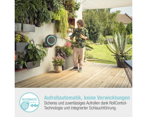 Gartenszene mit einer Person, die einen Gartenschlauch mit Aufrollautomatik von Gardena benutzt, vor einer bepflanzten Wand.