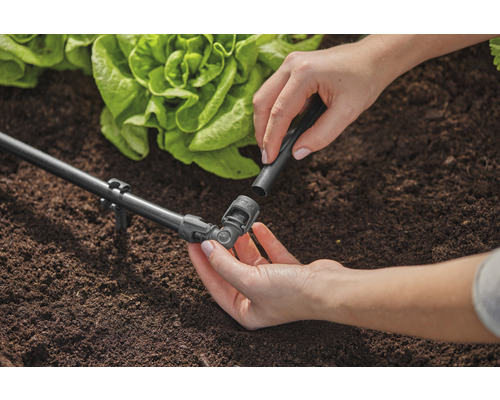 Gartenszene mit Bewässerungssystem und Person, die ein Verbindungsstück anbringt.