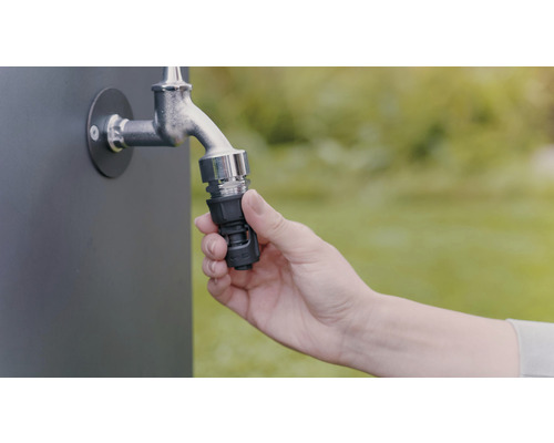 Eine Hand befestigt einen Schlauchverbinder an einem Wasserhahn für die Gartenbewässerung.