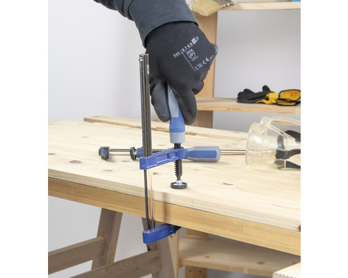 Eine Schraubzwinge fixiert zwei Holzstücke auf einer Werkbank.