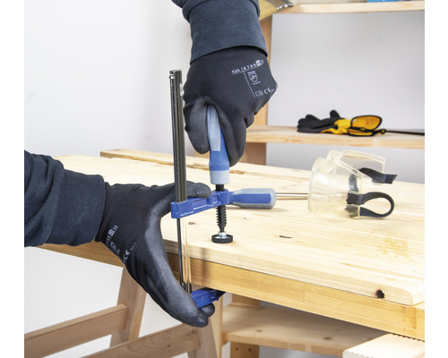 Eine Person befestigt mit einer Einhandzwinge zwei Holzbretter auf einer Werkbank.