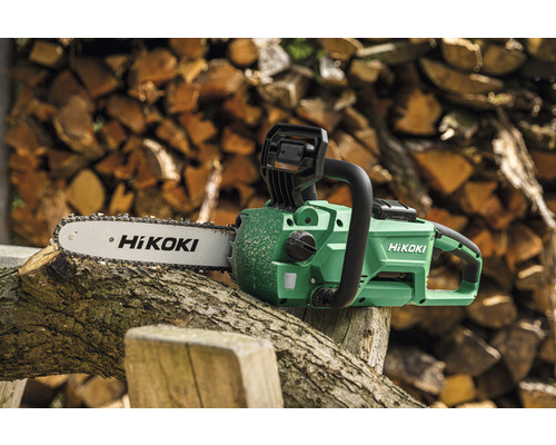 Hikoki Akku-Kettensäge auf einem Baumstamm vor Holzstapel