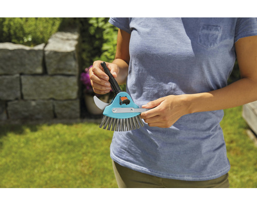 Eine Person hält eine Fugenkratzer-Bürste mit Fugenkratzer und Bürste.