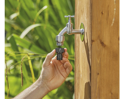 Eine Hand schließt einen Wasserhahnverbinder an einen Wasserhahn im Garten an.
