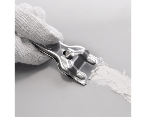 Eine Hand mit einem weißen Handschuh hält einen Spachtel aus Metall, der Spachtelmasse auf einer Oberfläche verteilt.