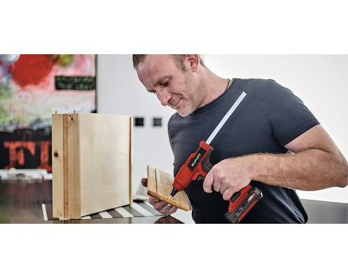 Mann verwendet eine Heißklebepistole zum Zusammenfügen von Holzteilen.