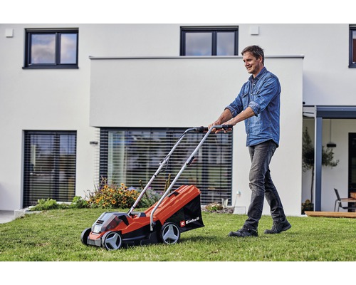Ein Mann benutzt einen Rasenmäher von Einhell im Garten vor einem Wohnhaus.