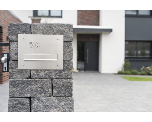 Briefkastenanlage aus Edelstahl an einer Steinmauer vor einem Wohnhaus
