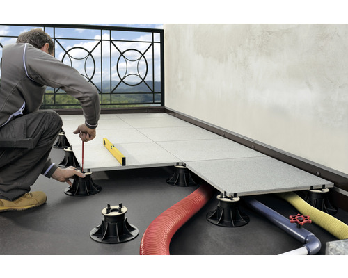 Mann verlegt Terrassenplatten auf einem Balkon mit Hilfe von Stelzlagern