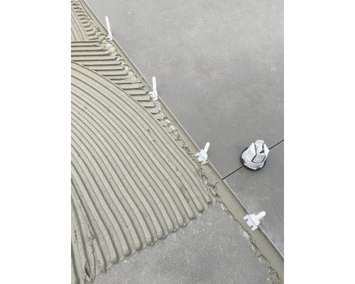 Fliesenlegerwerkzeug mit Nivelliersystem auf frischem Kleber zwischen Fliesen