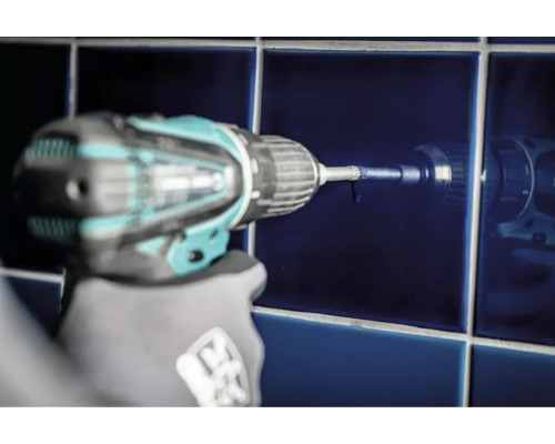 Eine Bohrmaschine bohrt ein Loch in eine blaue Fliese.