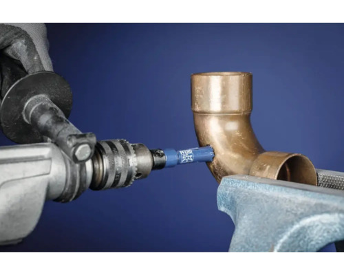 Eine Lochsäge bohrt ein Loch in ein Kupferrohr, das in einem Schraubstock befestigt ist