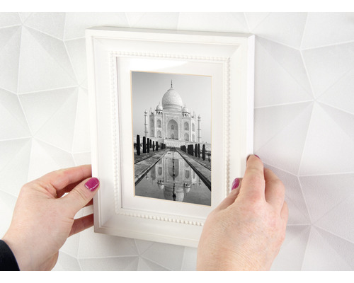 Hände halten einen weißen Bilderrahmen mit einem Schwarzweißfoto des Taj Mahal vor einer Wand