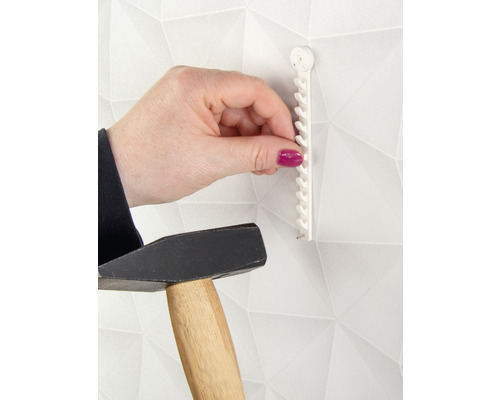 Eine Person befestigt einen Bilderhaken mit einem Hammer an einer Wand