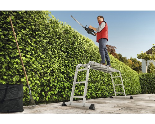 Mann schneidet Hecke mit Heckenschere von einem Gerüst aus