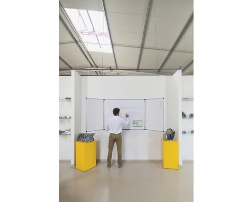 Mann schreibt auf eine dreiteilige, weisse Magnettafel in einem hellen Raum.